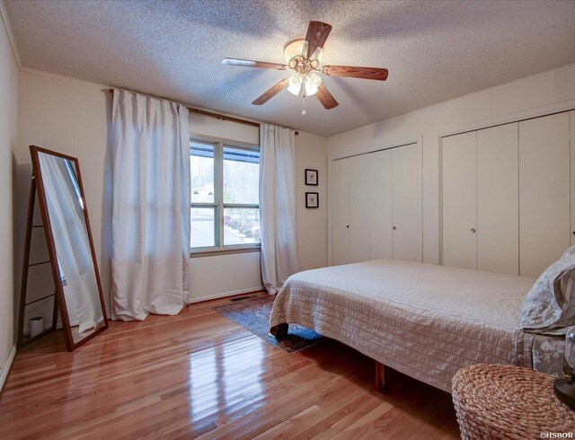 bedroom featuring light wood-type flooring, ceiling fan, a textured ceiling, and two closets