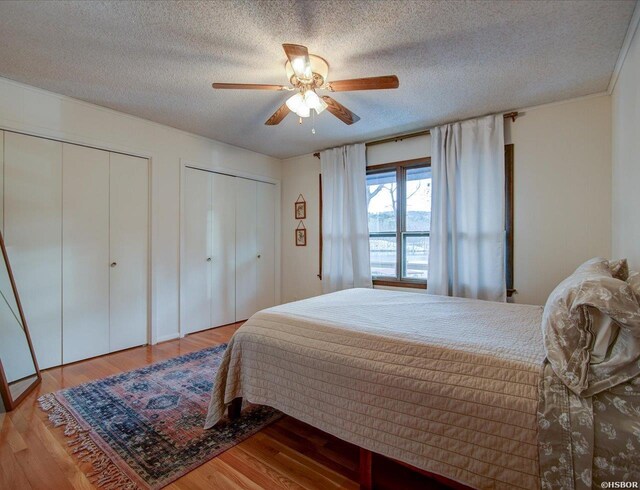 bedroom with a ceiling fan, two closets, a textured ceiling, and wood finished floors