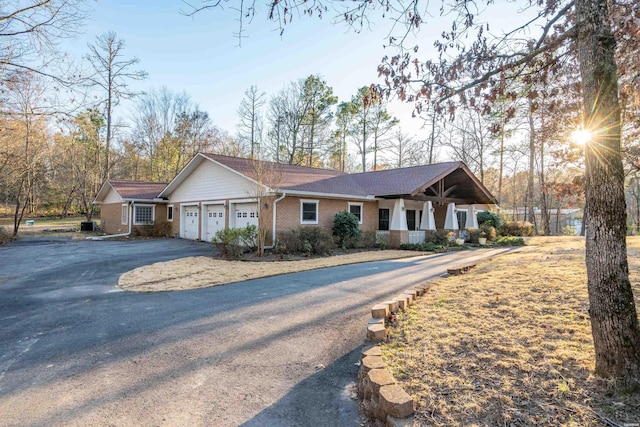 ranch-style house featuring an attached garage, covered porch, aphalt driveway, and brick siding