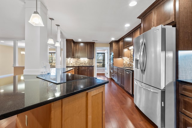 kitchen with tasteful backsplash, dark wood-style floors, dark stone countertops, hanging light fixtures, and stainless steel appliances