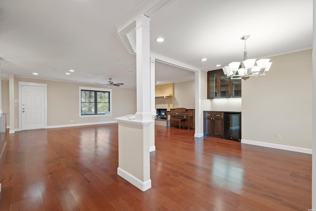 interior space featuring a large fireplace, beverage cooler, baseboards, dark wood-style floors, and ceiling fan with notable chandelier