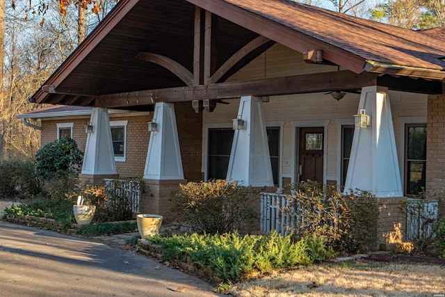 view of exterior entry with a porch, brick siding, and roof with shingles