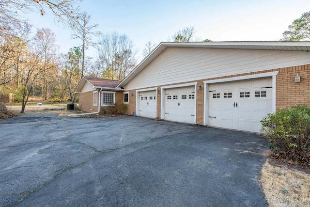 view of side of property with central air condition unit, an attached garage, aphalt driveway, and brick siding