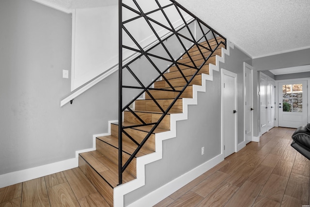 staircase featuring ornamental molding, a textured ceiling, baseboards, and wood finished floors