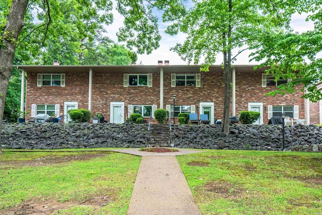 view of front facade with brick siding, a chimney, and a front yard