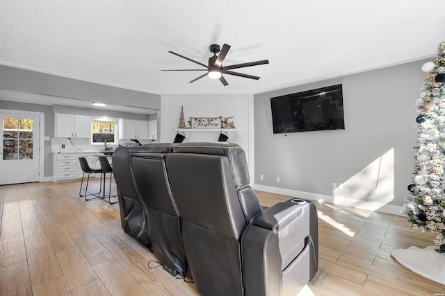 living room featuring a ceiling fan, light wood-type flooring, a textured ceiling, and baseboards