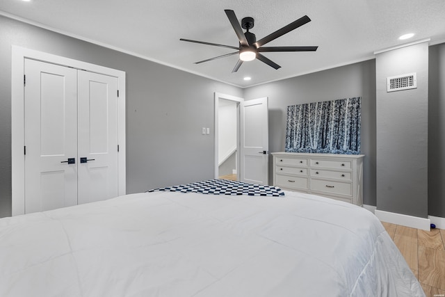 bedroom featuring light wood finished floors, a closet, visible vents, and crown molding