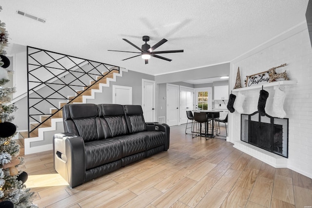 living area with a textured ceiling, a fireplace, visible vents, light wood-style floors, and stairs