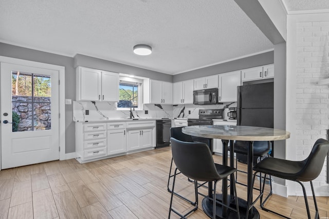 kitchen featuring a sink, white cabinets, light countertops, light wood-type flooring, and black appliances