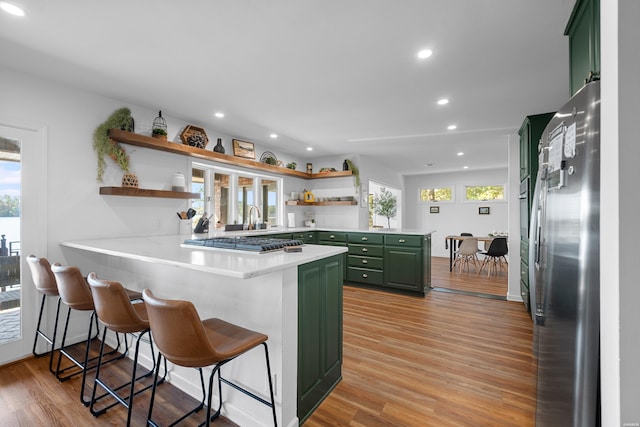 kitchen featuring a peninsula, stainless steel appliances, green cabinets, light countertops, and open shelves