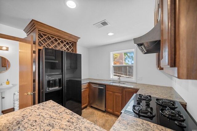 kitchen featuring range hood, visible vents, brown cabinetry, a sink, and black appliances