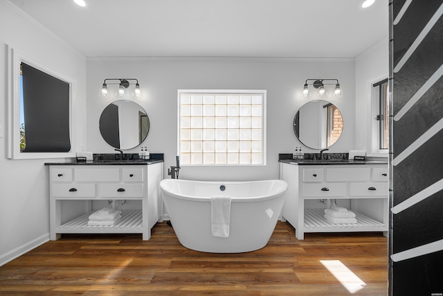 bathroom with ornamental molding, a soaking tub, two vanities, and wood finished floors