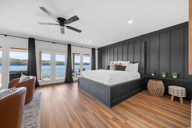 bedroom with a decorative wall, a water view, light wood-style floors, access to exterior, and french doors