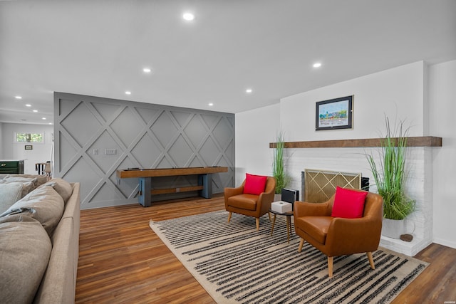 living area featuring a brick fireplace, an accent wall, wood finished floors, and recessed lighting