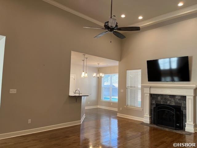 unfurnished living room featuring crown molding, a premium fireplace, dark wood-type flooring, ceiling fan, and baseboards