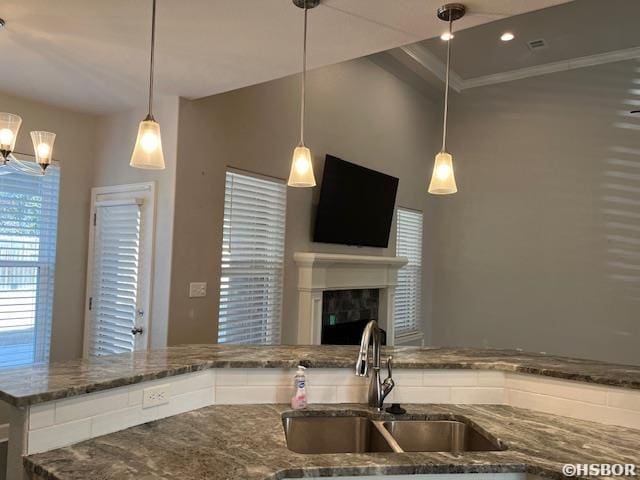 kitchen with a fireplace, a sink, hanging light fixtures, dark stone counters, and crown molding