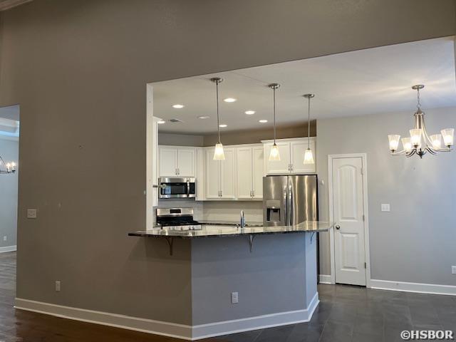 kitchen with appliances with stainless steel finishes, a breakfast bar, white cabinetry, and pendant lighting