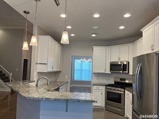 kitchen featuring stainless steel appliances, a sink, white cabinets, hanging light fixtures, and dark stone countertops