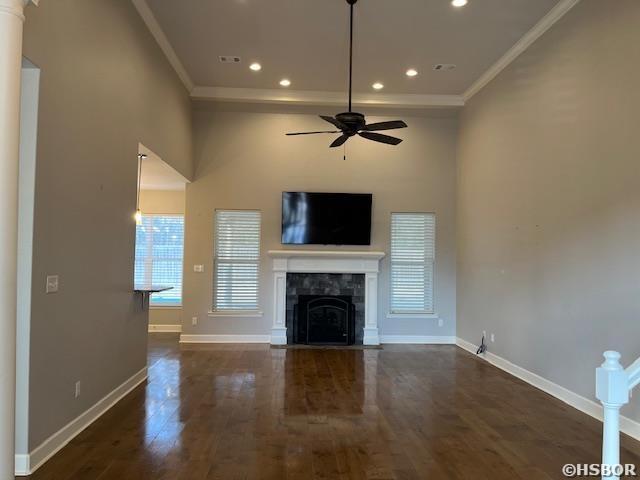 unfurnished living room with dark wood-style floors, a fireplace with flush hearth, a ceiling fan, ornamental molding, and baseboards