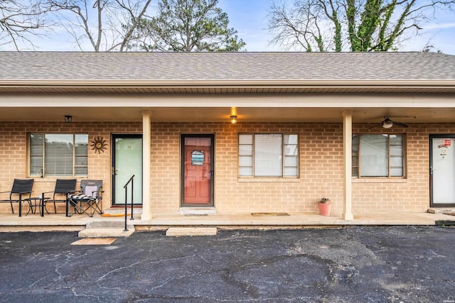 doorway to property featuring a shingled roof, a porch, and brick siding