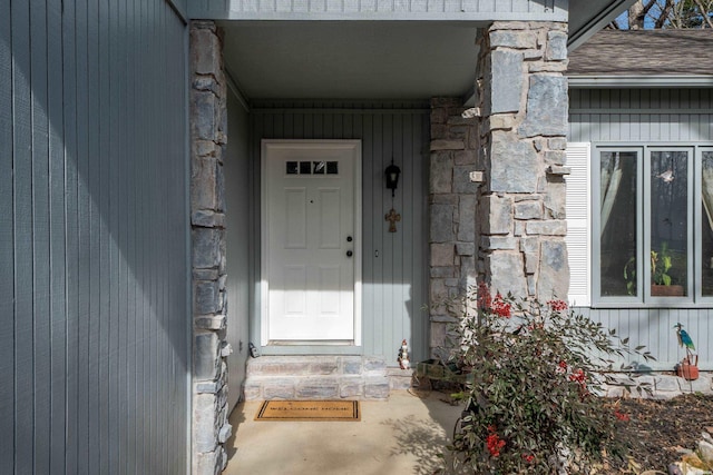 view of exterior entry featuring stone siding and roof with shingles