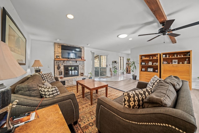 living area with a ceiling fan, beamed ceiling, wood finished floors, a stone fireplace, and recessed lighting