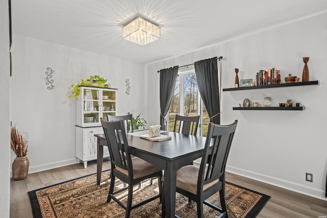 dining area with dark wood-style flooring, a notable chandelier, and baseboards