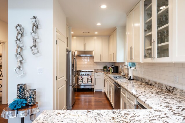 kitchen with white cabinets, glass insert cabinets, appliances with stainless steel finishes, light stone countertops, and under cabinet range hood