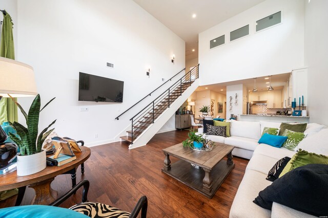 living room with visible vents, baseboards, dark wood-style floors, stairway, and a high ceiling