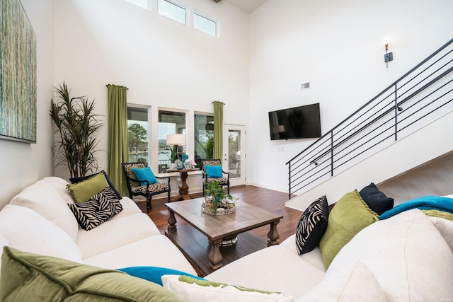 living room featuring visible vents, a towering ceiling, wood finished floors, baseboards, and stairs