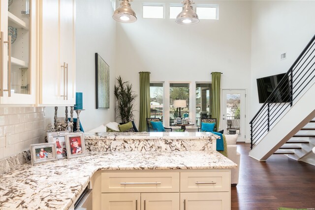 kitchen with light stone counters, dark wood-type flooring, a towering ceiling, glass insert cabinets, and pendant lighting