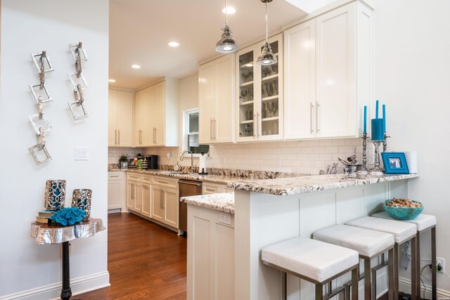 kitchen with a peninsula, a breakfast bar, a sink, light stone countertops, and glass insert cabinets