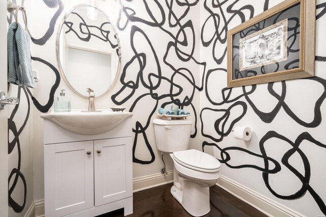 half bathroom featuring baseboards, vanity, toilet, and wood finished floors