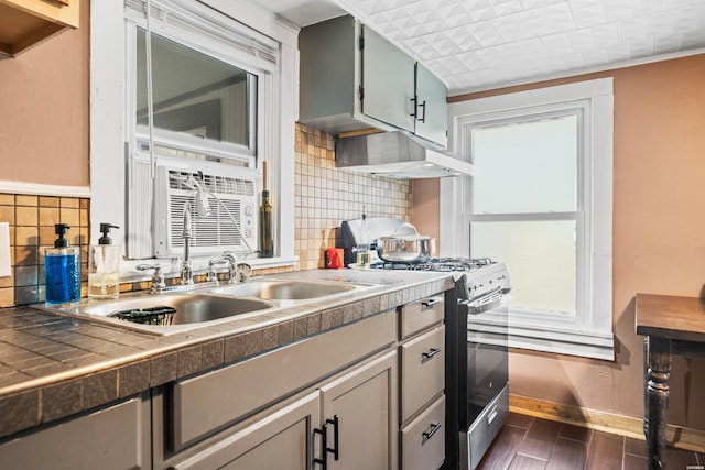 kitchen with dark wood finished floors, gray cabinetry, stainless steel range with gas stovetop, ventilation hood, and baseboards