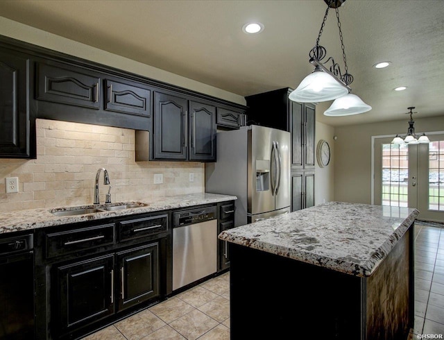 kitchen with a kitchen island, light stone counters, stainless steel appliances, pendant lighting, and a sink