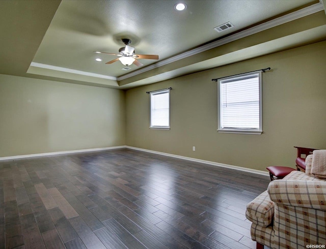 unfurnished room featuring a raised ceiling, dark wood-type flooring, ornamental molding, ceiling fan, and baseboards