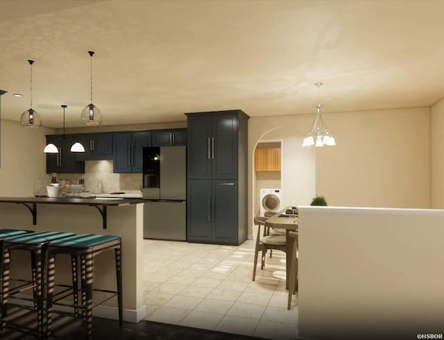 kitchen featuring arched walkways, freestanding refrigerator, dark countertops, a kitchen bar, and washer / dryer