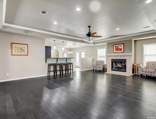 living area featuring a raised ceiling, visible vents, dark wood finished floors, and baseboards