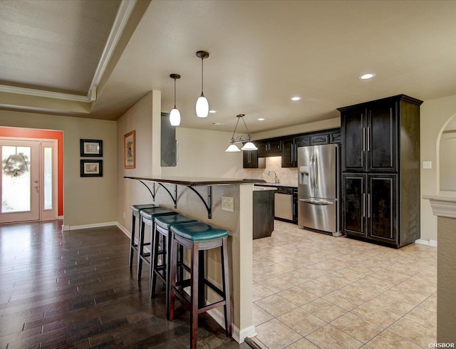 kitchen featuring a kitchen breakfast bar, stainless steel appliances, crown molding, pendant lighting, and a sink