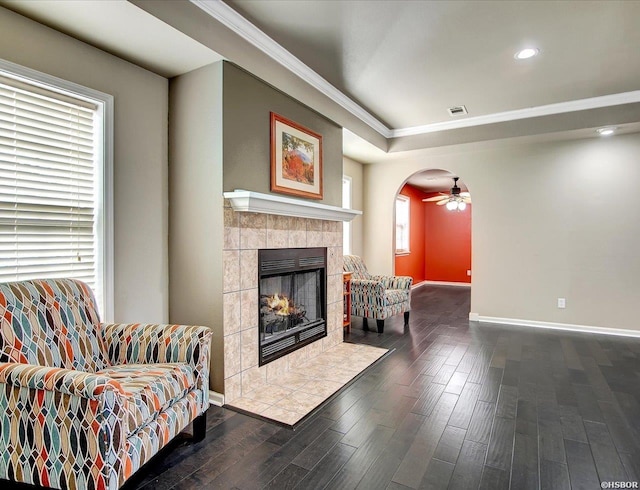 living area featuring visible vents, arched walkways, a tiled fireplace, dark wood-type flooring, and crown molding