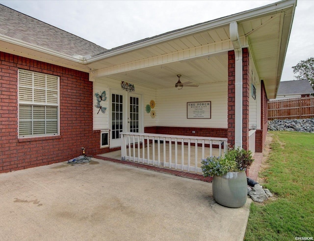 view of exterior entry featuring brick siding, a shingled roof, a porch, ceiling fan, and fence