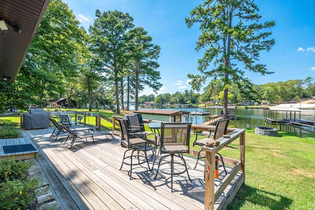 wooden deck with a water view, an outdoor fire pit, and a lawn