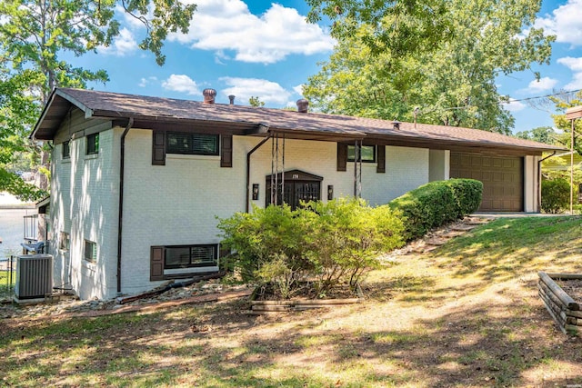 back of property featuring an attached garage, central AC unit, and brick siding