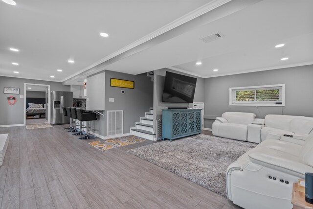 living room with ornamental molding, visible vents, and light wood-style flooring