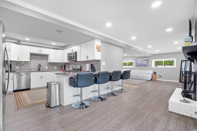 kitchen featuring a breakfast bar, appliances with stainless steel finishes, open floor plan, white cabinets, and a sink