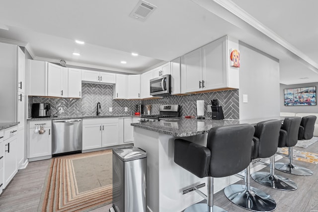 kitchen featuring stainless steel appliances, a peninsula, white cabinetry, visible vents, and a kitchen breakfast bar