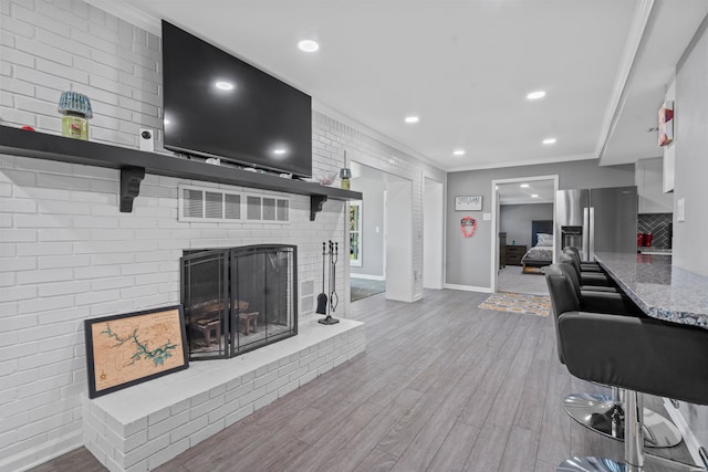 living area with light wood finished floors, visible vents, crown molding, a fireplace, and recessed lighting