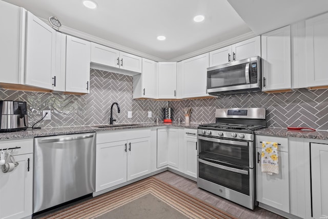 kitchen with stainless steel appliances, backsplash, stone countertops, white cabinetry, and a sink