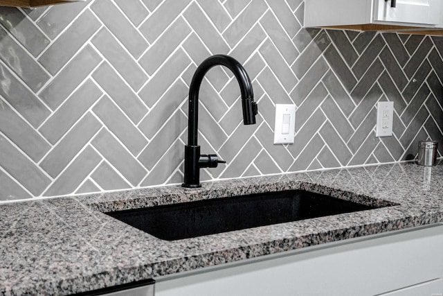 room details featuring light stone counters, a sink, white cabinetry, and decorative backsplash