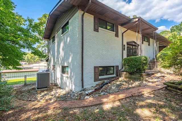 view of side of property with central AC unit, fence, and brick siding